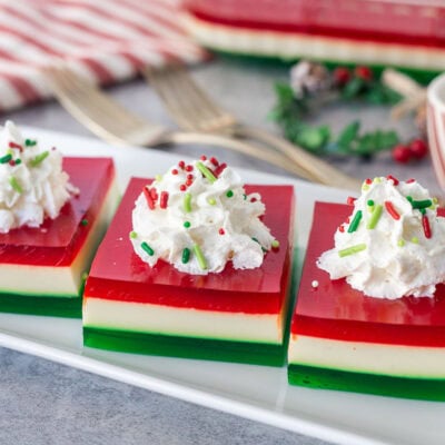 Three slices of Christmas Jell-O salad on a plate with whipped cream and sprinkles.