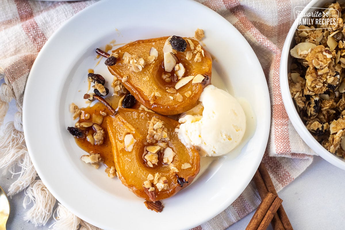 Two baked pear slices on a plate with granola and vanilla ice cream.