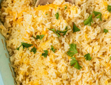 Casserole dish of cheesy rice with parsley and a wooden spoon.