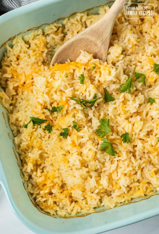 Casserole dish of cheesy rice with parsley and a wooden spoon.