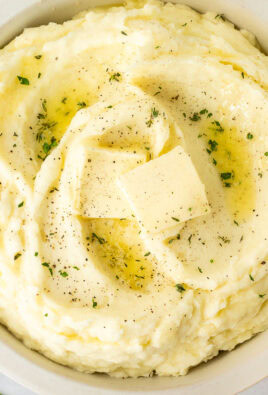 Bowl of mashed potatoes with fresh herbs, pepper, and butter.