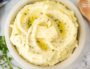 Bowl of mashed potatoes with fresh herbs, pepper, and butter.