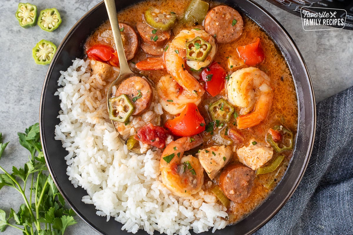 A black serving dish filled with Instant Pot Gumbo and Rice. Shrimp, sausage, chicken, peppers, and vegetables are visible in the gumbo.