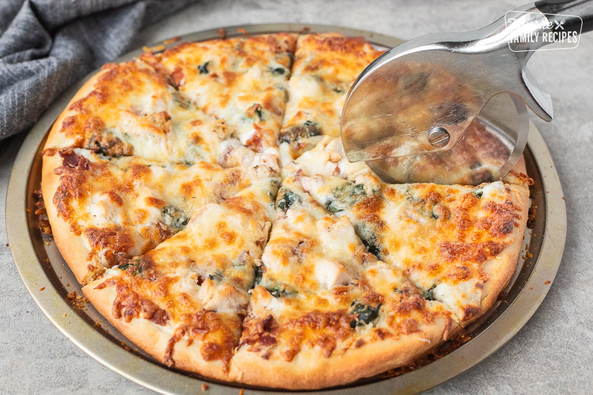 Cutting Alfredo pizza with a pizza slicer.