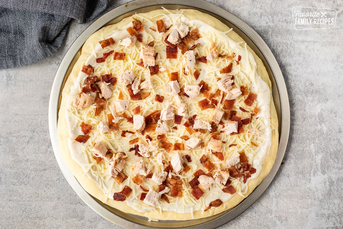 Pizza with bacon and chicken on top of Alfredo sauce and cheese.