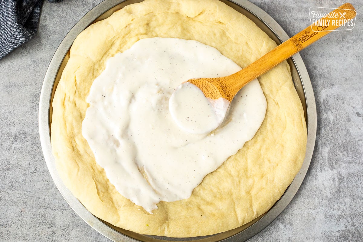 Spreading Alfredo sauce on cooked pizza crust.