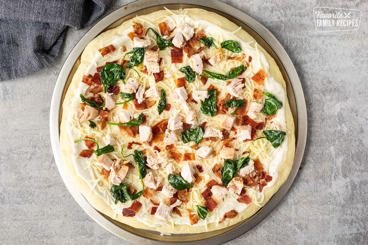 Spinach added to Alfredo pizza with bacon, chicken and cheese.