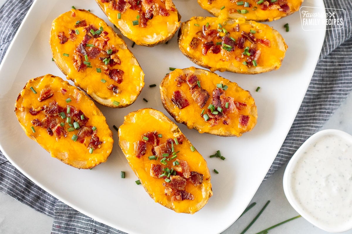 Loaded potato skins on a platter with bacon, cheese and chives. Bowl of Ranch on the side.