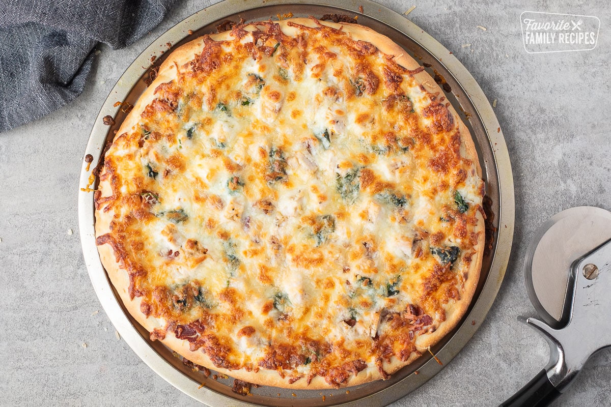 Baked Alfredo pizza on a pizza pan. Pizza cutter on the side.