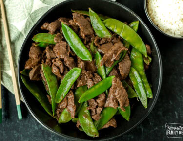 Beef with snow peas in a serving bowl next to a small bowl of rice