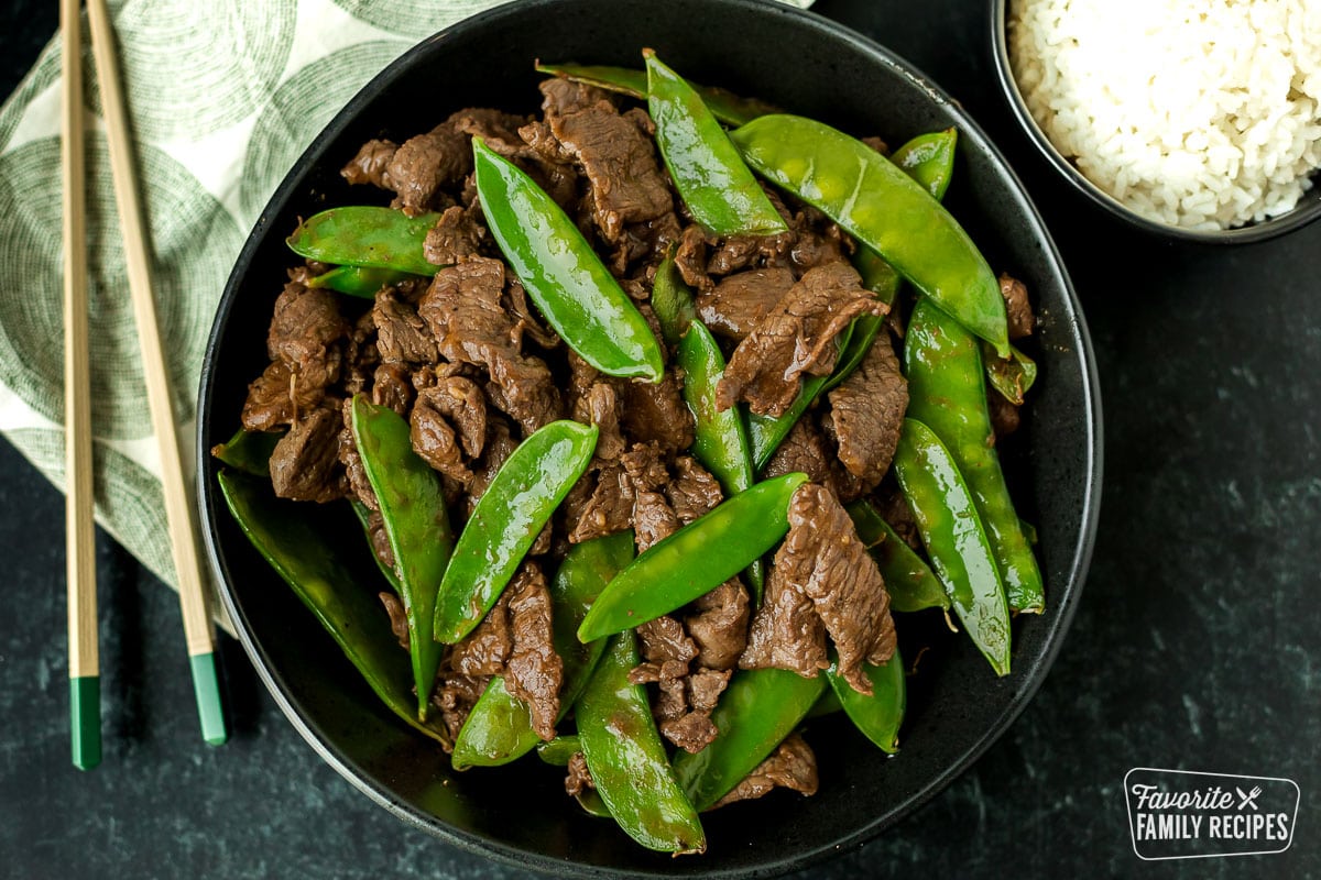 Beef with snow peas in a serving bowl next to a small bowl of rice