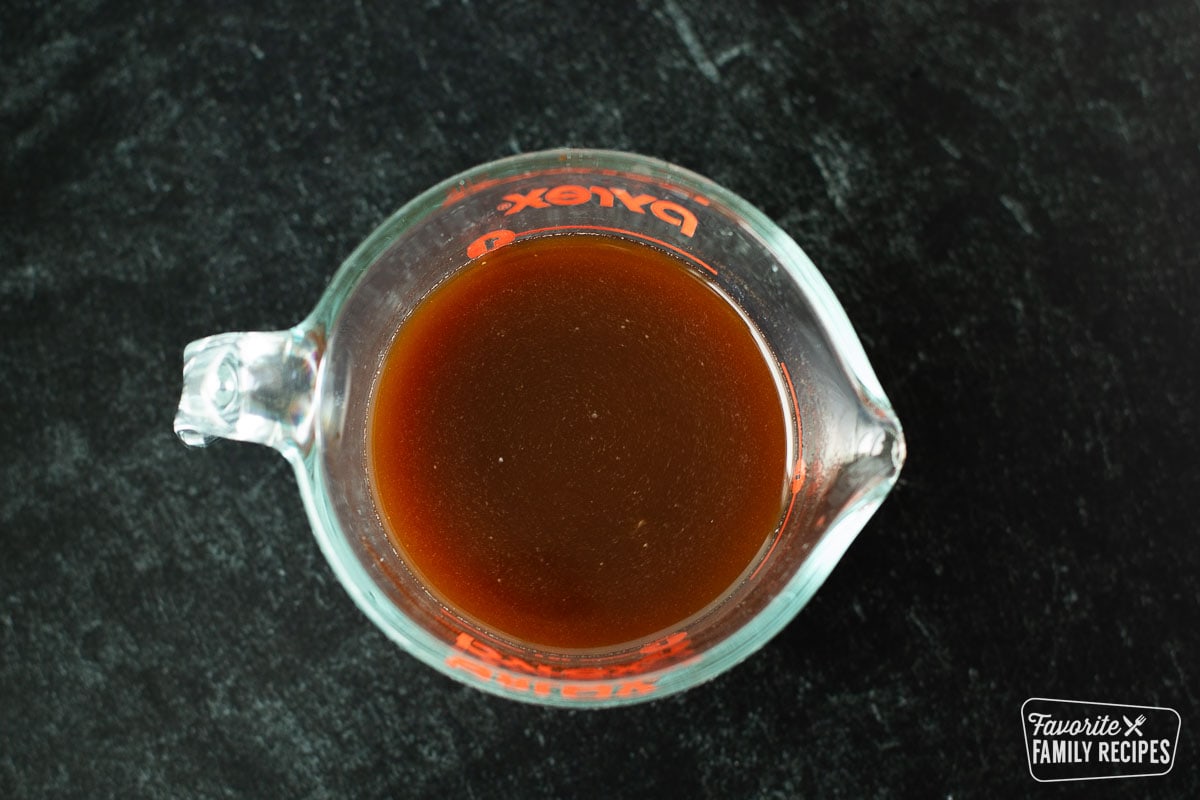 A marinade of beef broth, soy sauce, and garlic in a glass measuring cup