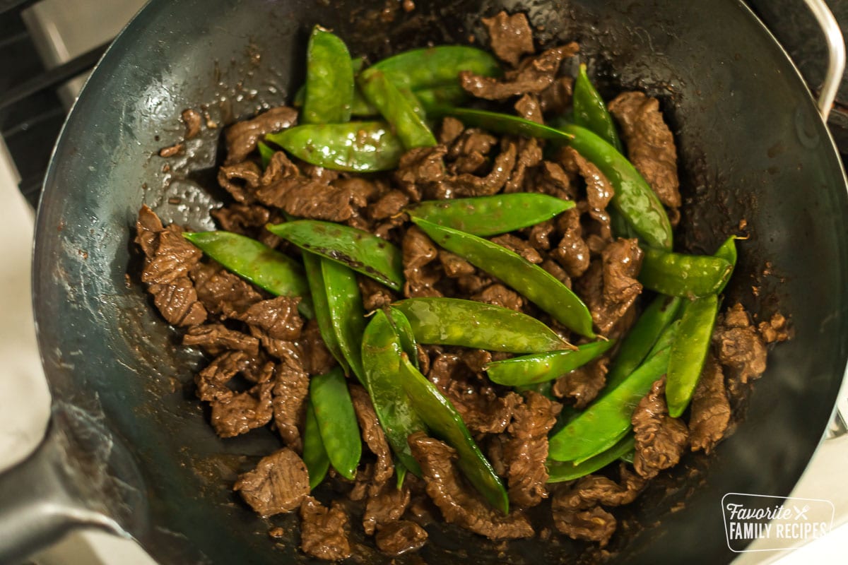 Beef and snow peas in a wok cooking on a stovetop