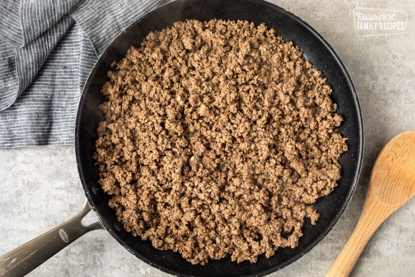 Skillet with ground beef and wooden spoon on the side.