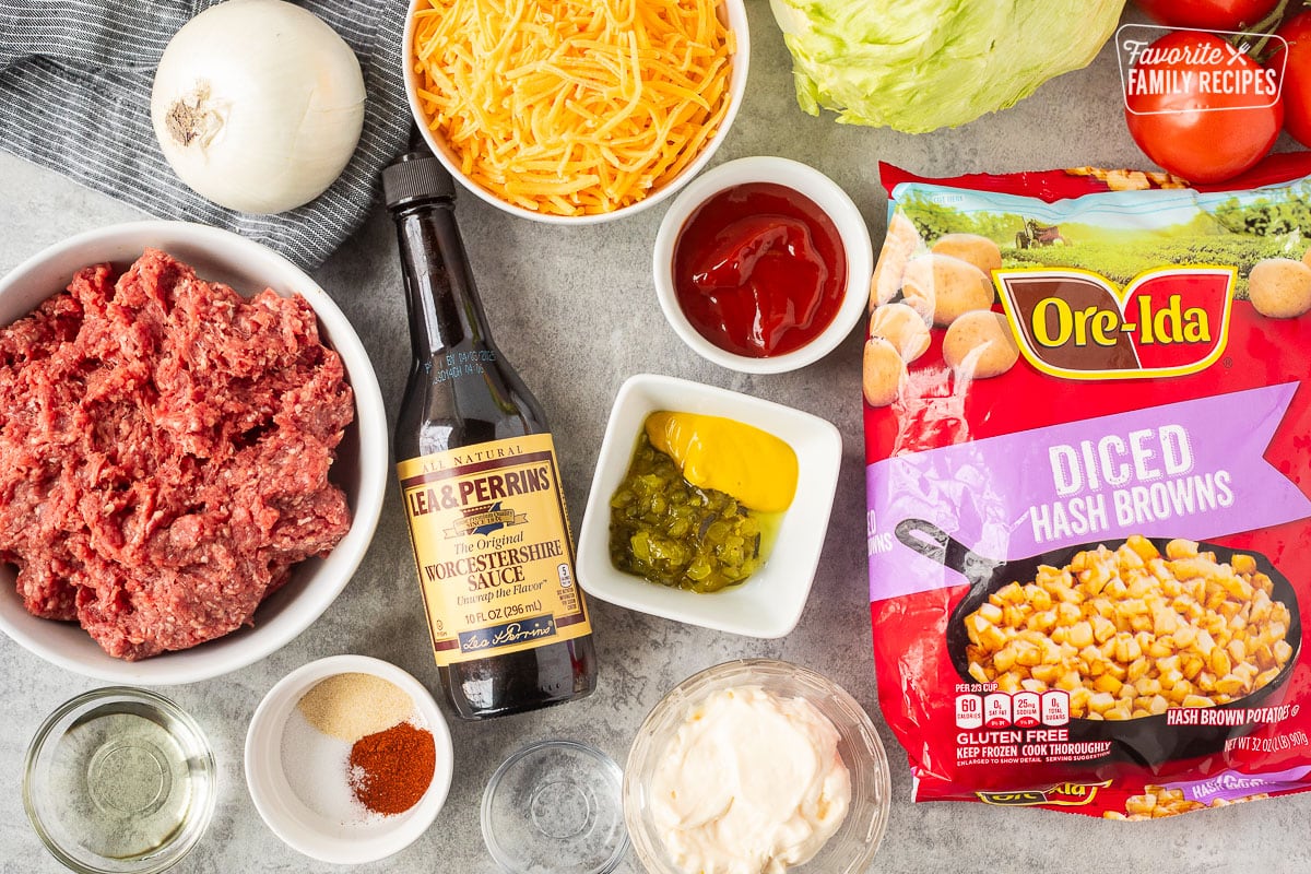 Ingredients to make big Mac casserole including hashbrowns, ketchup, mustard, relish, mayonnaise, vinegar, paprika, onion powder, salt, Worcestershire sauce, oil, ground beef, shredded cheddar cheese, white onion, tomatoes and lettuce.