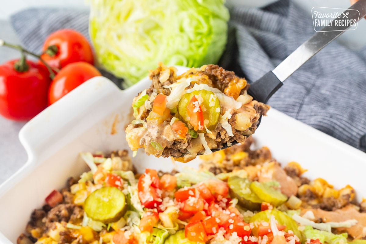 Scoop of Big Mac Casserole topped with lettuce, pickles, tomatoes and onion in a large spoon.