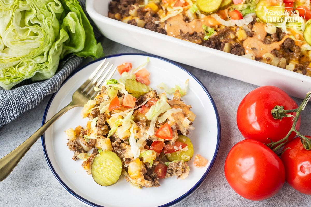 Plate with a serving of Big Mac Casserole topped with special sauce, lettuce, pickles, tomatoes and onions.