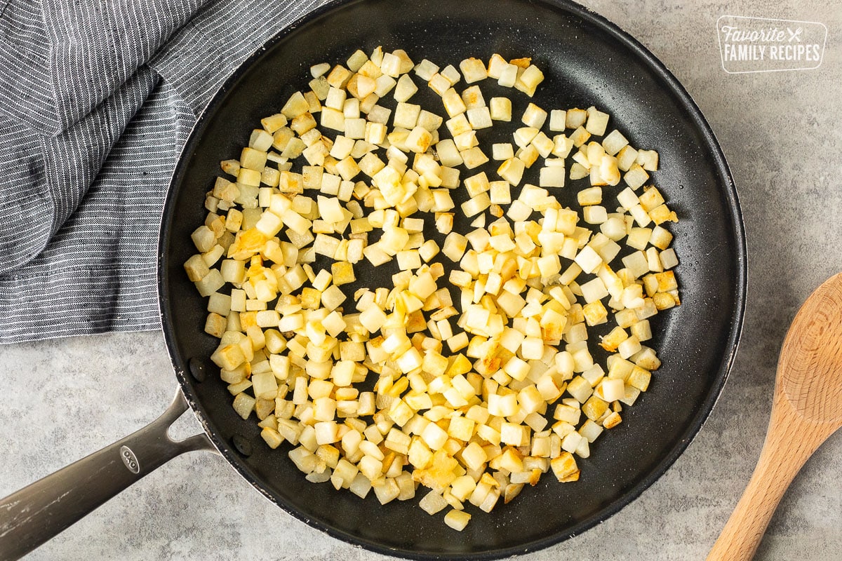 Skillet with cooked diced hash browns and wooden spoon on the side.