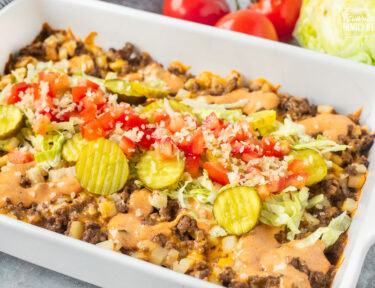 Casserole dish of Big Mac Casserole topped with pickles, lettuce, tomatoes and onions.