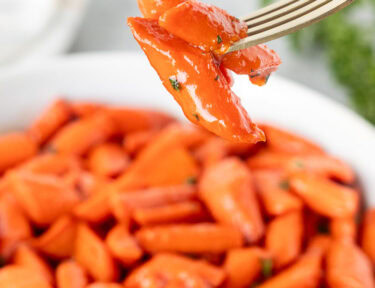 Fork with candied carrots over a bowl of candied carrots.