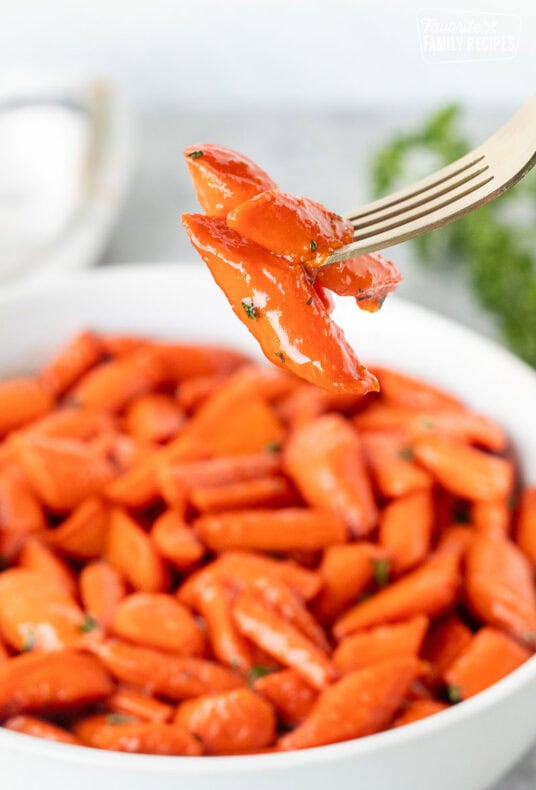 Fork with candied carrots over a bowl of candied carrots.