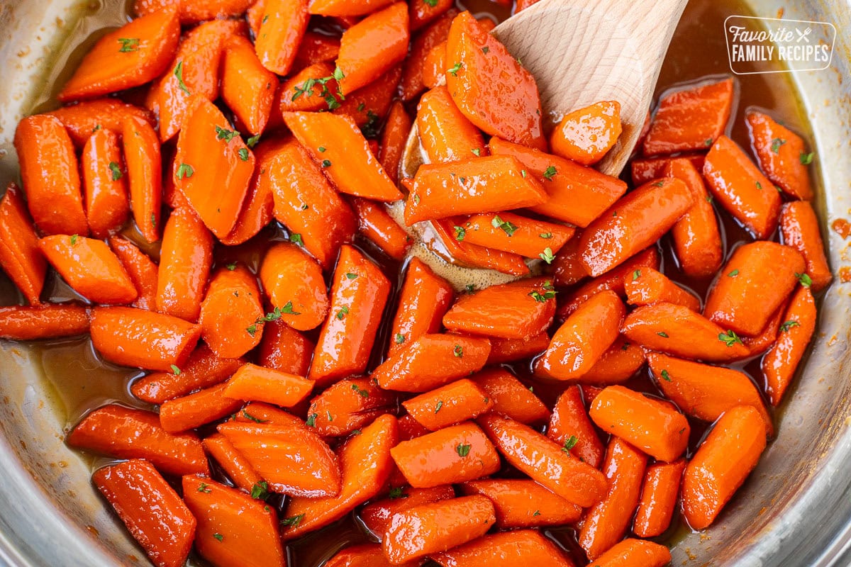 Candied carrots in a large skillet with wooden spoon.