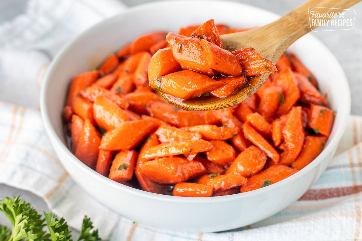 Spoon holding up a portion of candied carrots over a bowl of candied carrots.