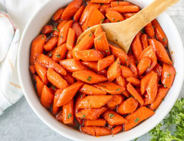 Bowl of candied carrots with a wooden spoon.