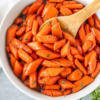 Bowl of candied carrots with a wooden spoon.