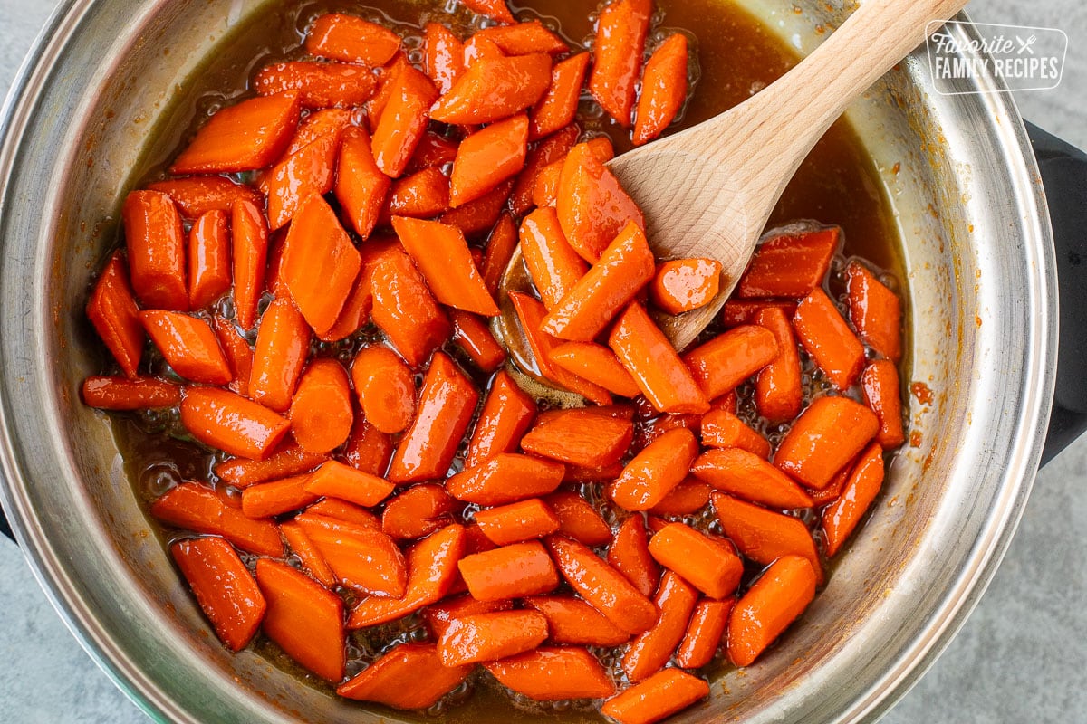 Candied carrots in a skillet with a wooden spoon.