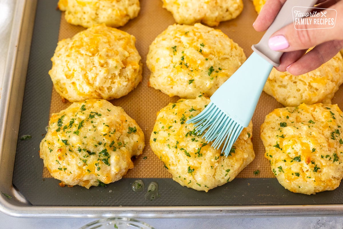 Brushing butter and parsley onto Cheddar Bay Biscuits.