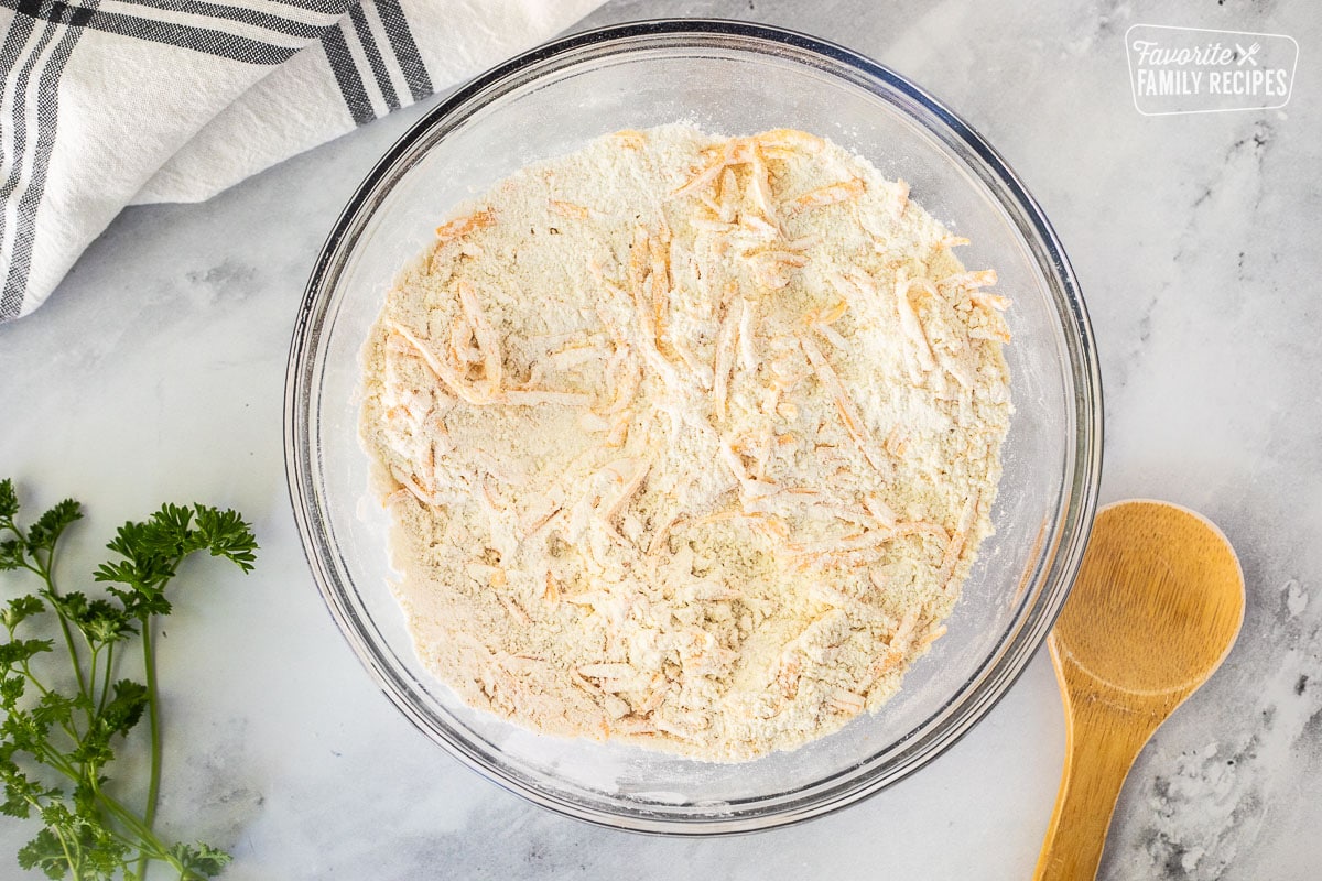 Glass mixing bowl with dry ingredients combined with cheese. Wooden spoon on the side.