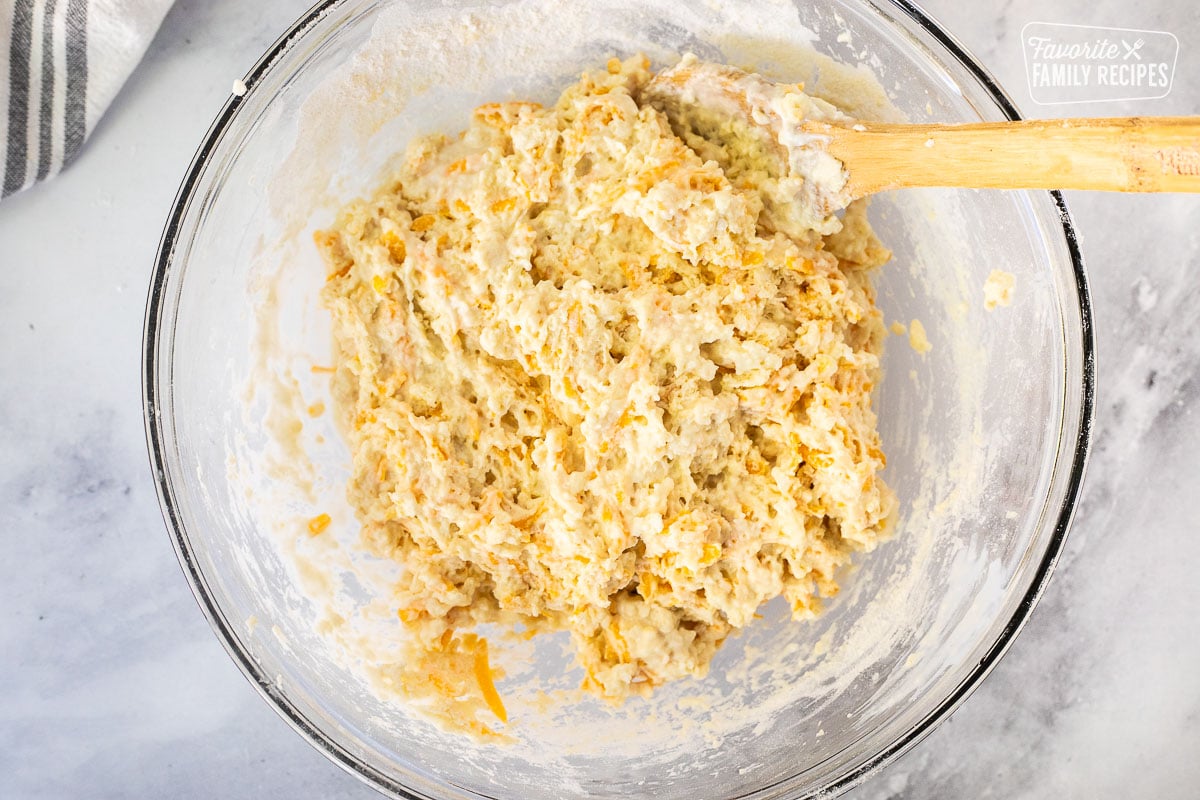 Cheddar Bay Biscuits dough in a glass mixing bowl with a wooden spoon.