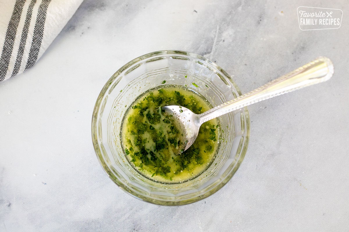 Glass mixing bowl with melted butter and parsley combined.