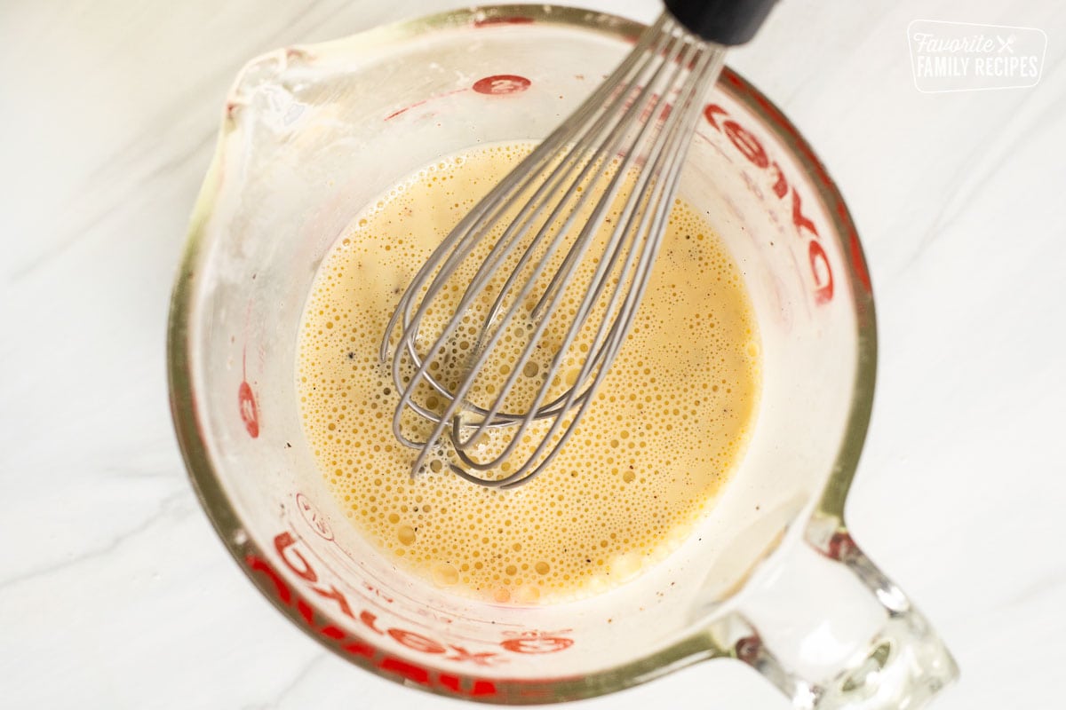 Mixing egg mixture with whisk in glass dish.