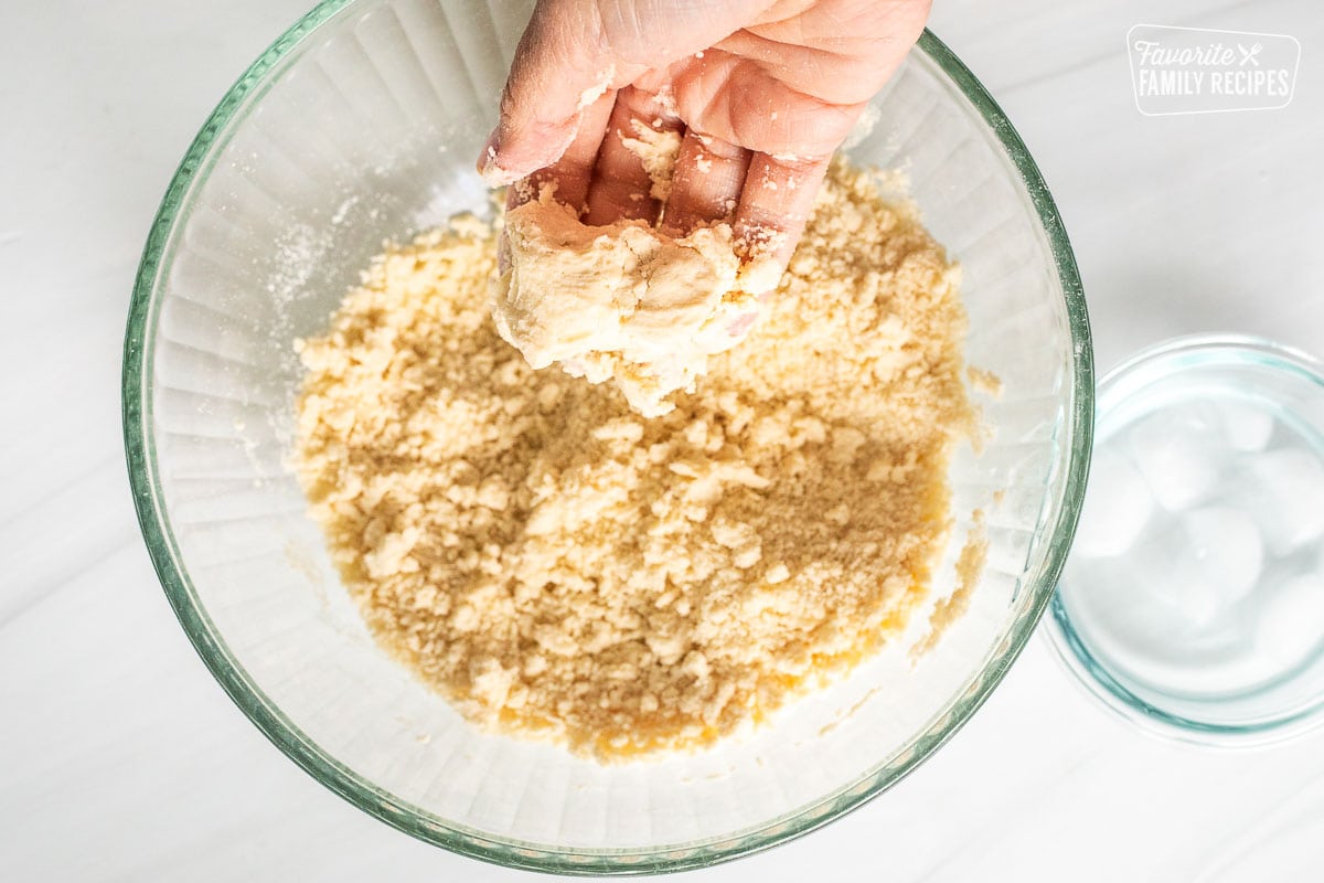 Hand holding pressed part of dough together over bowl.