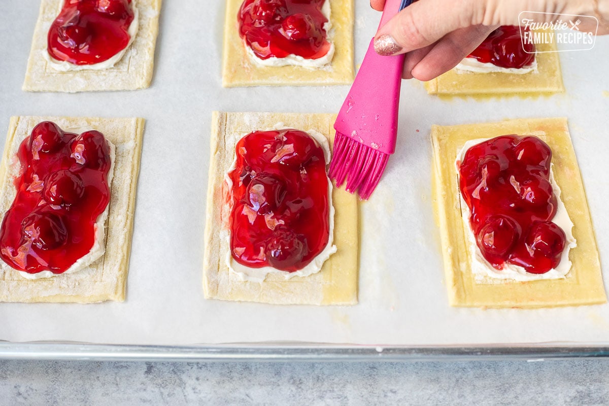 Brushing egg wash onto outside edge of unbaked cherry danish.