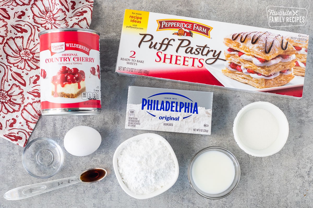 Ingredients to make Cherry danish, including puff pastry, sheets, cream, cheese, milk, sugar, egg, vanilla, water, and cherry pie filling in a can.