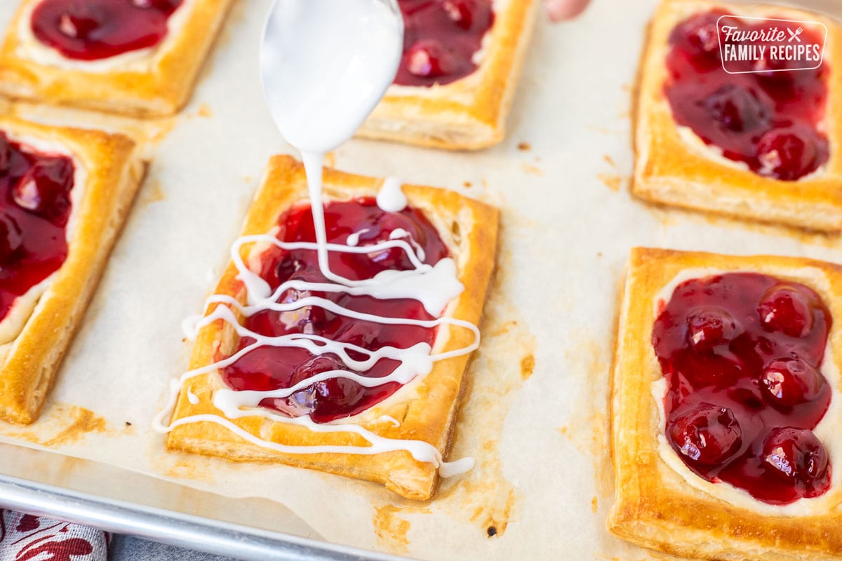 Spoon drizzling white icing onto baked cherry danish.