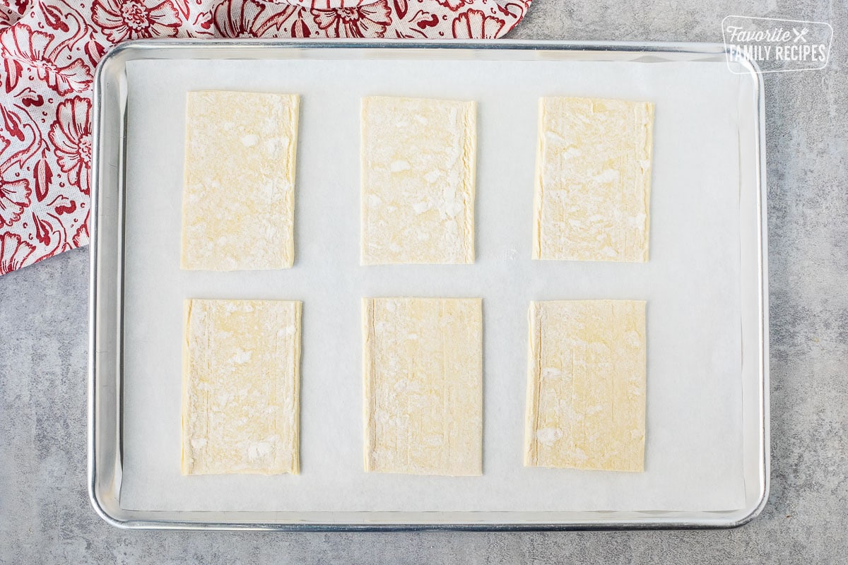 Baking sheet lined with parchment paper and six angled shaped puff pastry.