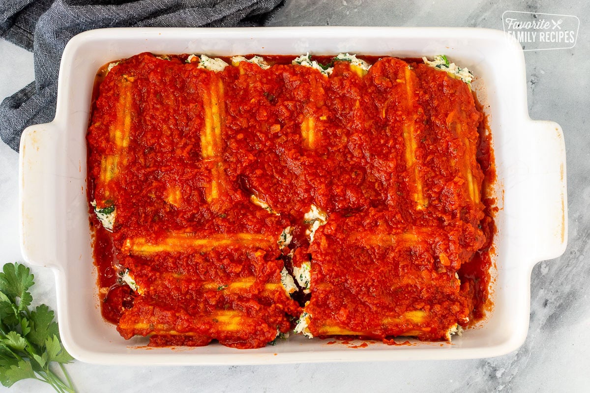 Baking dish with unbaked filled manicotti and topped with marinara sauce.