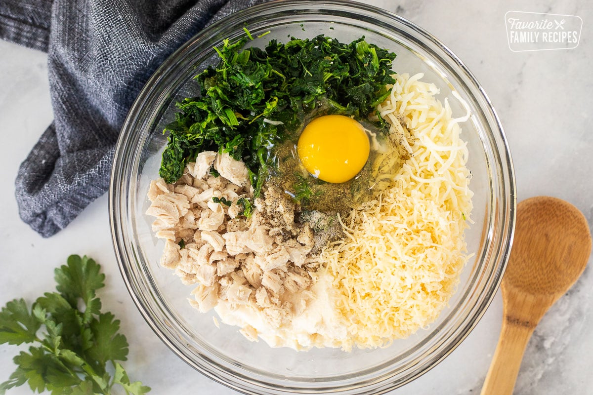 Glass bowl of ricotta cheese, mozzarella cheese. parmesan cheese. egg, spinach, chicken, salt and pepper.