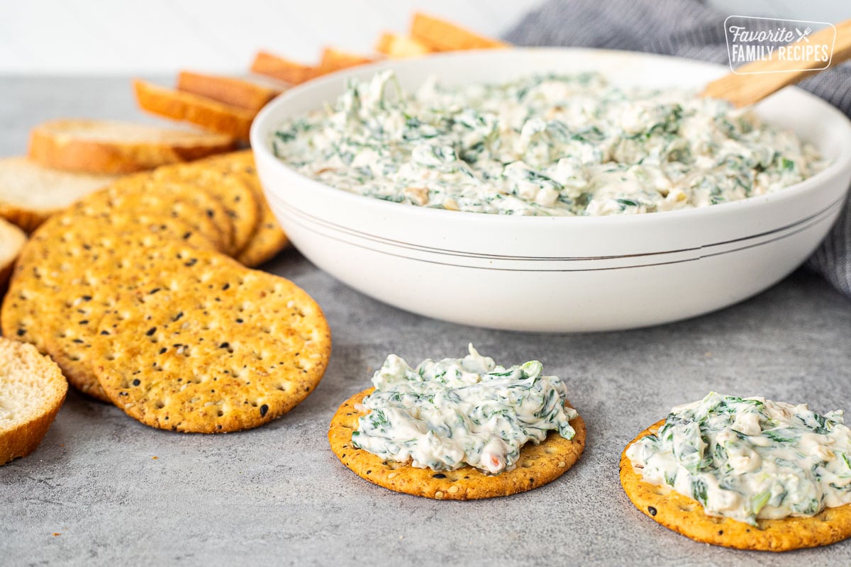 Easy spinach dip on two crackers next to a bowl of dip.