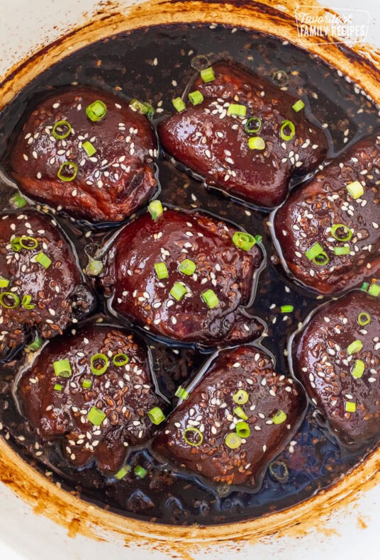 Crockpot with cooked Hawaiian chicken thighs, garnished with green onion and sesame seeds.