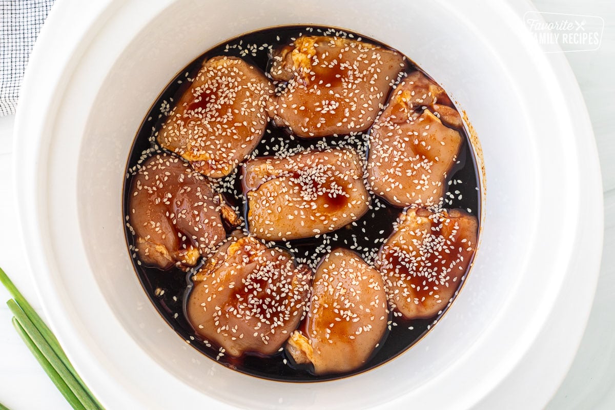 Crockpot with uncooked chicken thighs, Mr. Yoshida sauce and sesame seeds.