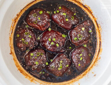 Crockpot with cooked Hawaiian chicken thighs, garnished with green onion and sesame seeds.