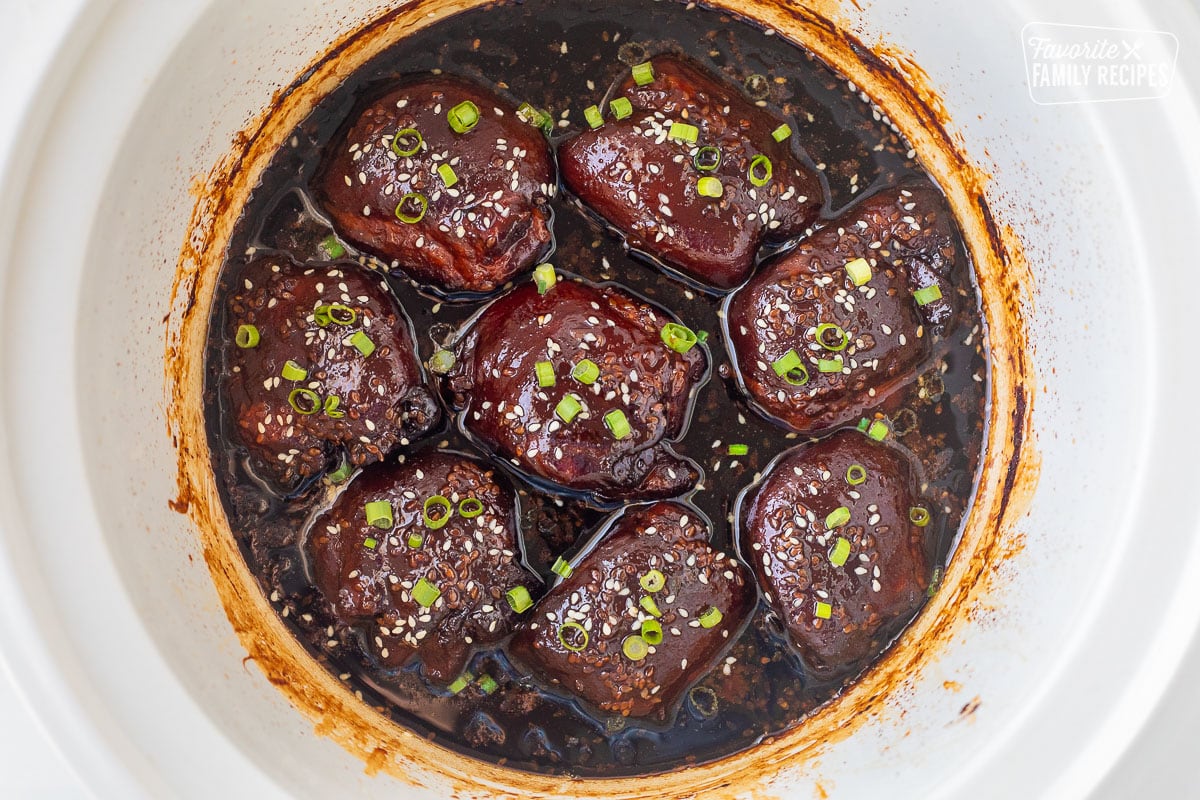 Crockpot with cooked Hawaiian chicken thighs, garnished with green onion and sesame seeds.