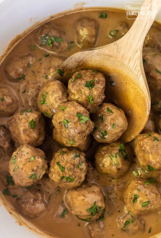 Spoon holding a scoop of Swedish Meatballs in a crock pot.