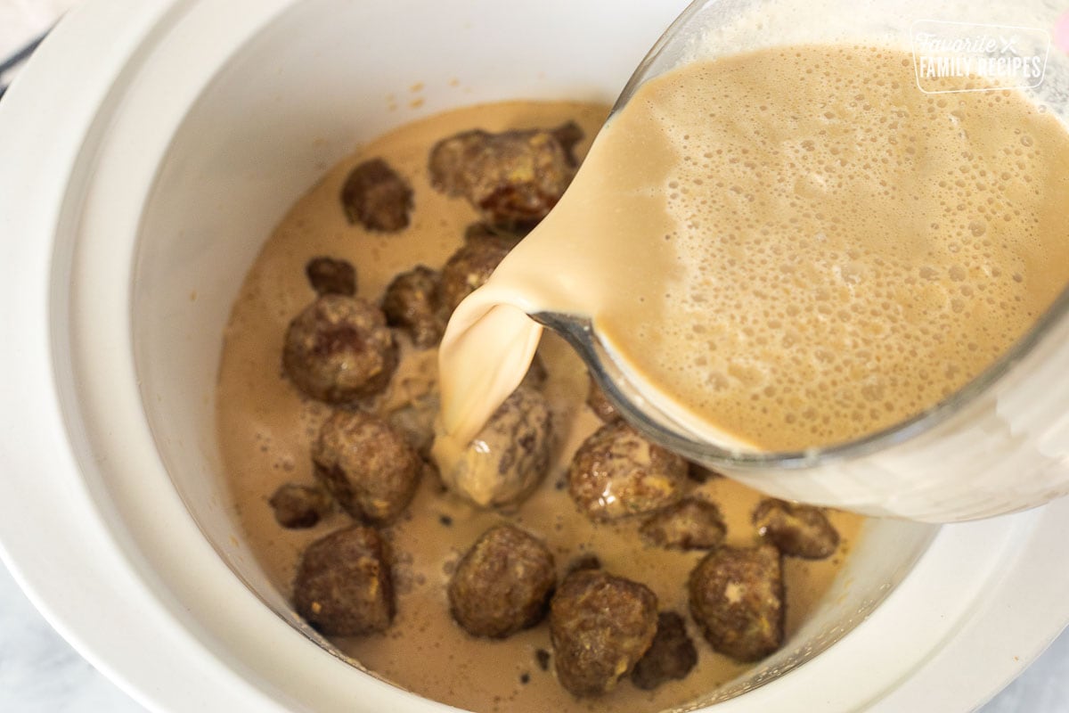 Pouring sauce in crock pot of cooked meatballs.