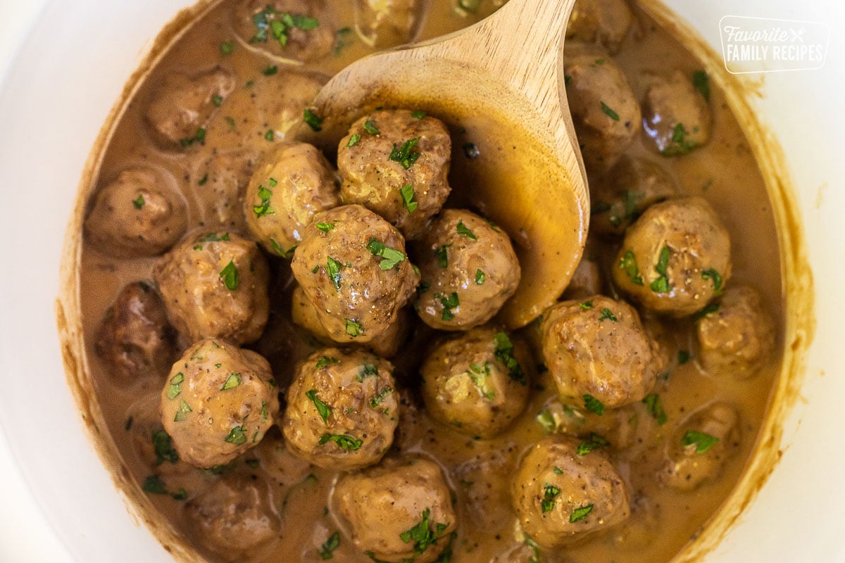 Spoon holding a scoop of Swedish Meatballs in a crock pot.